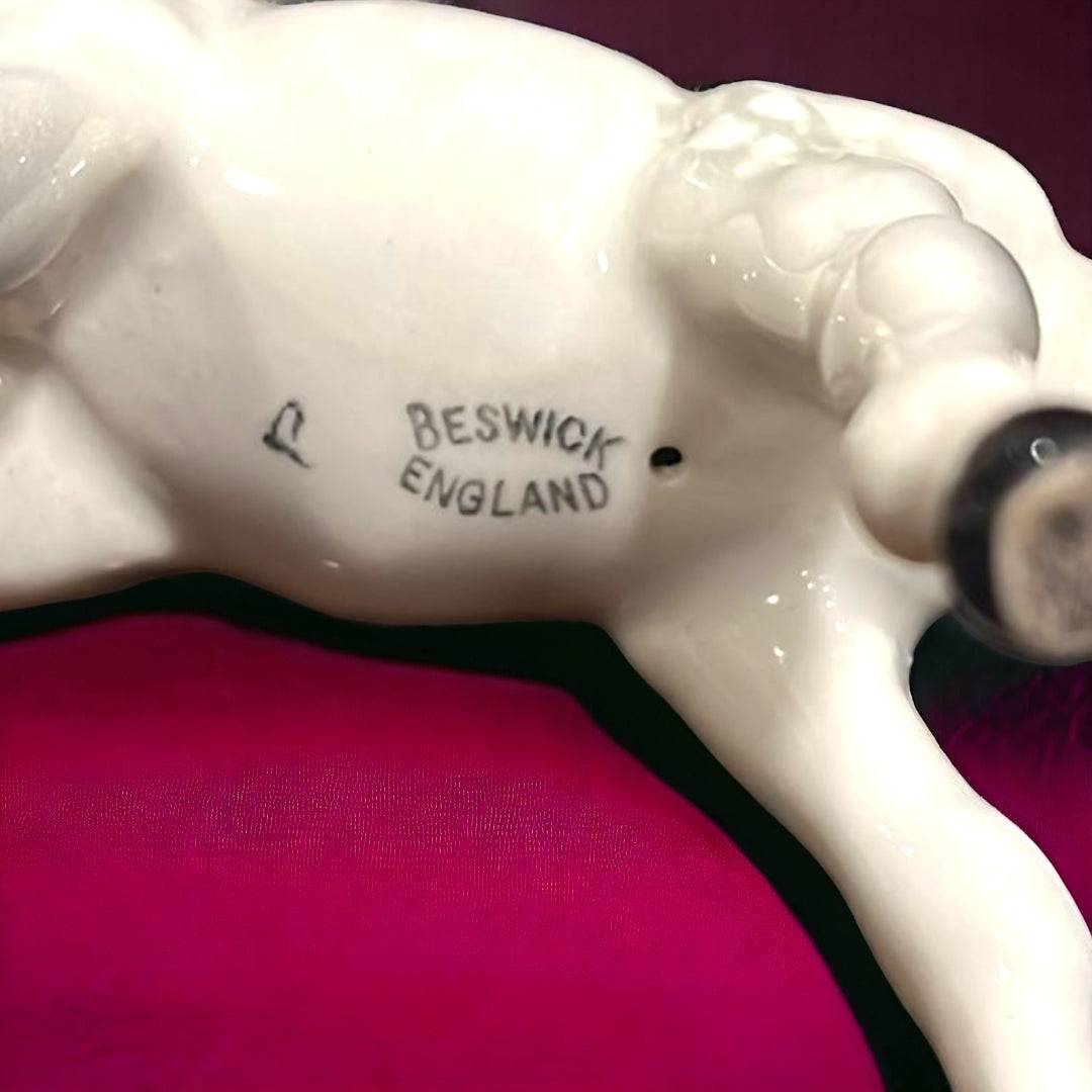 Caballo de porcelana Beswick en posición de pastar, acabado blanco brillante sobre fondo burdeos. Elegancia inglesa para coleccionistas de decoración.