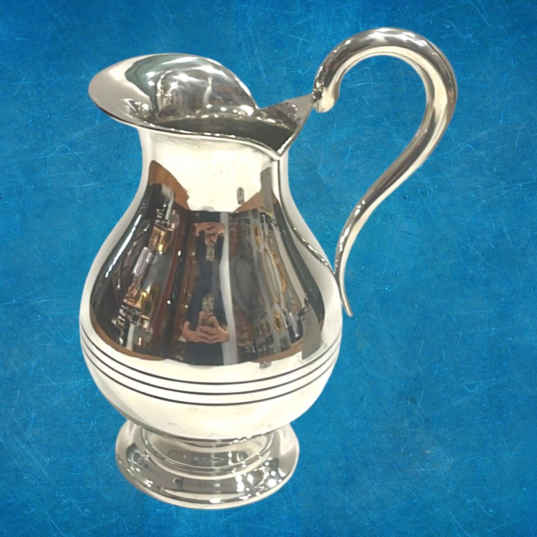 Jarra de metal plateado elegante con diseño moderno, acabado pulido y mango curvado, ideal para decoración o servir bebidas.