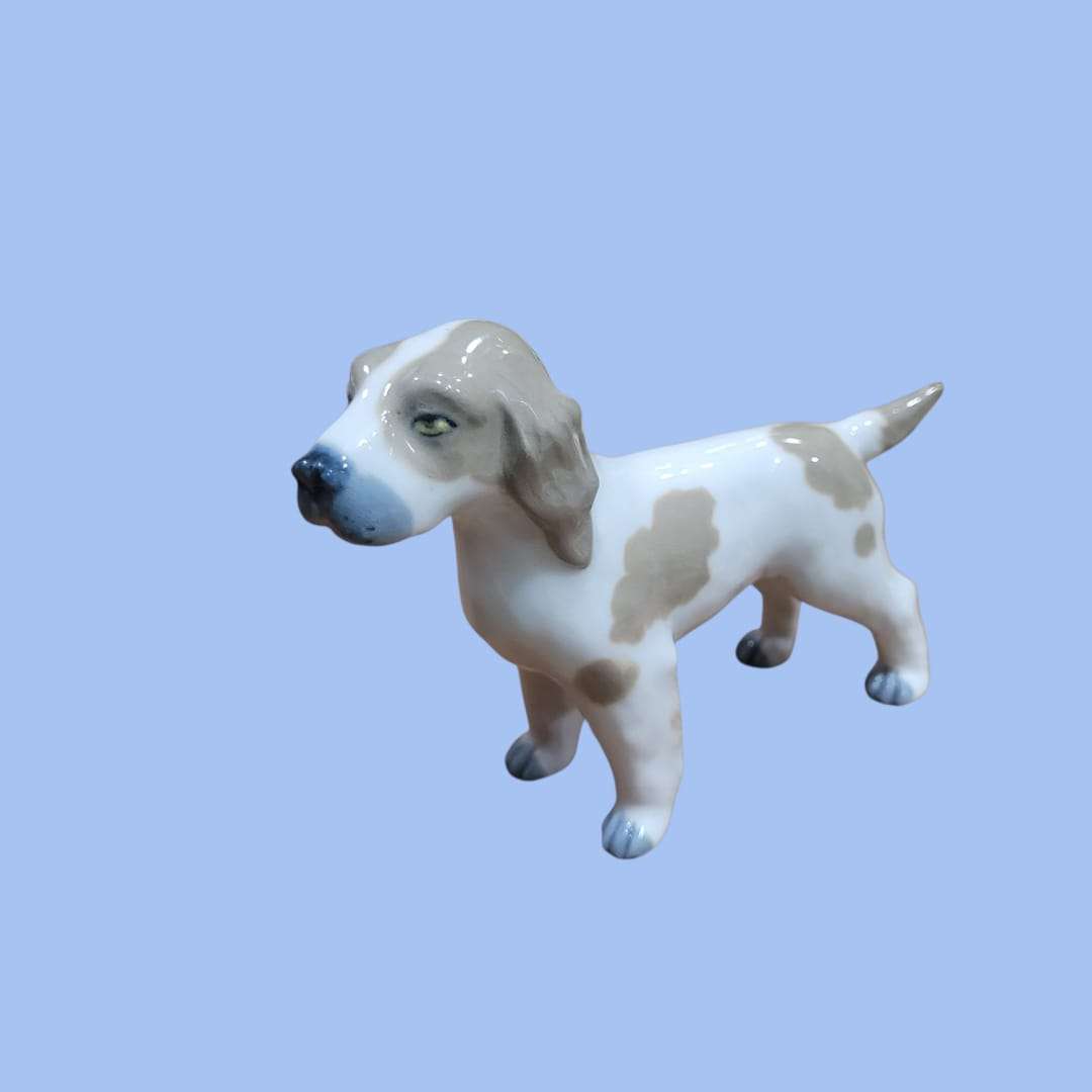 Perro de porcelana Lladró, pieza decorativa exclusiva con acabado brillante y detalles artesanales en tonos beige y blanco. Ideal para decoración de interiores.