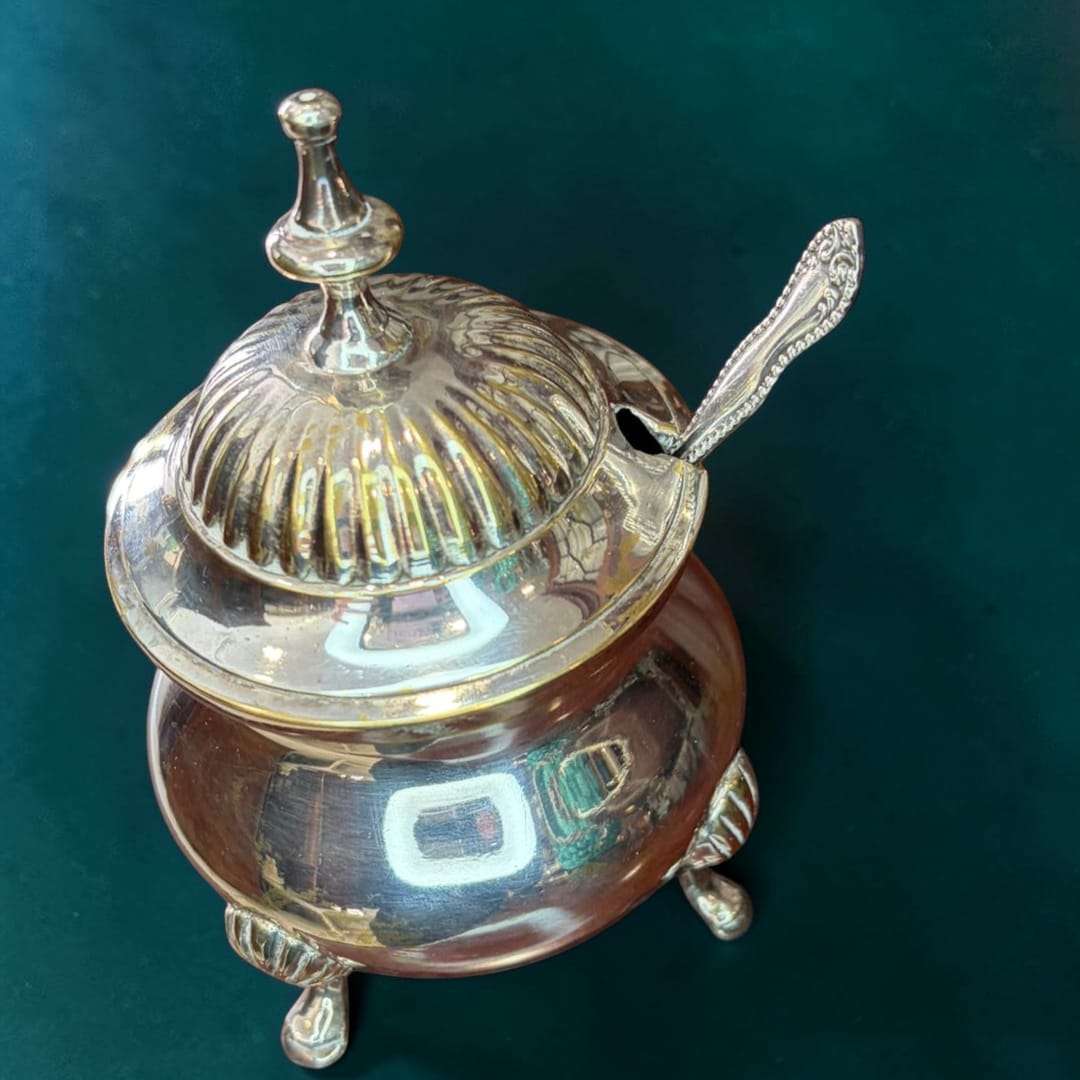 Este azucarero de metal plateado es una pieza de sobremesa concebida originalmente para guardar y servir azúcar de forma limpia, elegante y práctica durante el servicio de café, té o desayuno.
