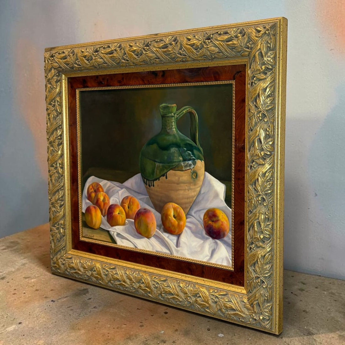 Este bodegón al óleo firmado J.M. Sampalo representa una composición de jarra y frutas sobre una tela blanca. 