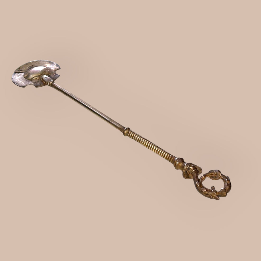 Badila de bronce antigua para brasero tradicional con diseño funcional y decorativo, ideal para manipulación de brasas en decoración rústica.