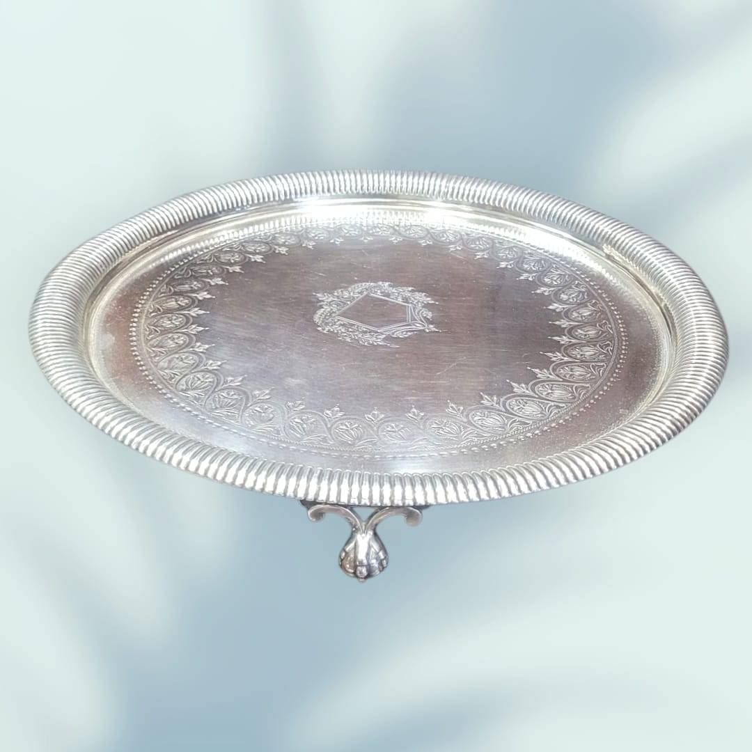 Bandeja de metal plateado con ornamentos elegantes, diseño floral en relieve y escudo central, ideal para decoración vintage de interiores.
