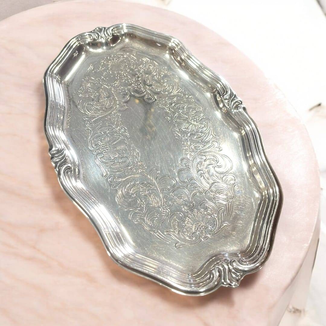 Bandeja de metal plateado con bordes curvos y grabados decorativos vintage. Perfecta para servir con estilo o ambientar espacios retro.