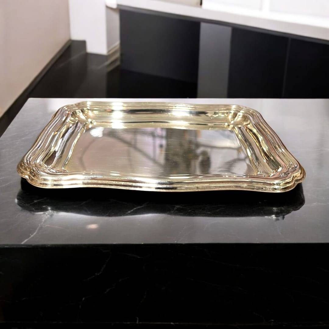 Bandeja de metal plateado con diseño ondulado clásico sobre superficie de mármol negro. Ideal para decoración elegante en el hogar.