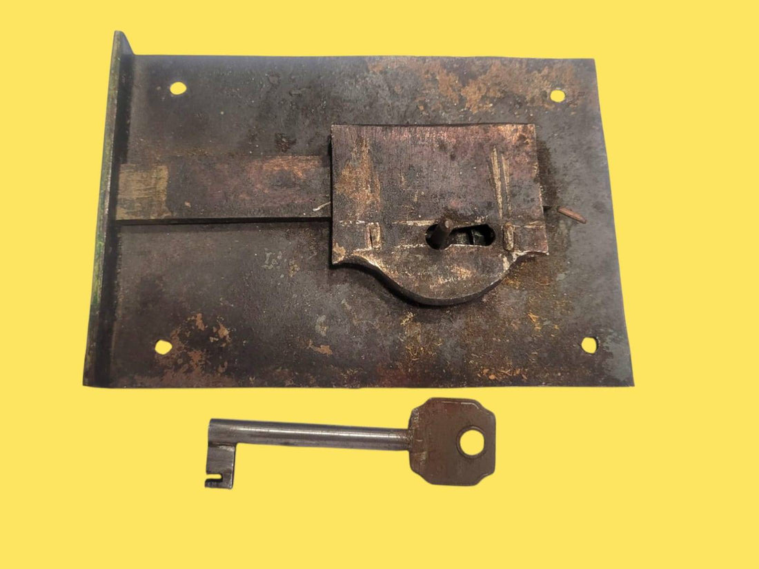 Cerradura de forja antigua con llave original sobre fondo amarillo. Ideal para decoración rústica o restauración de puertas vintage.