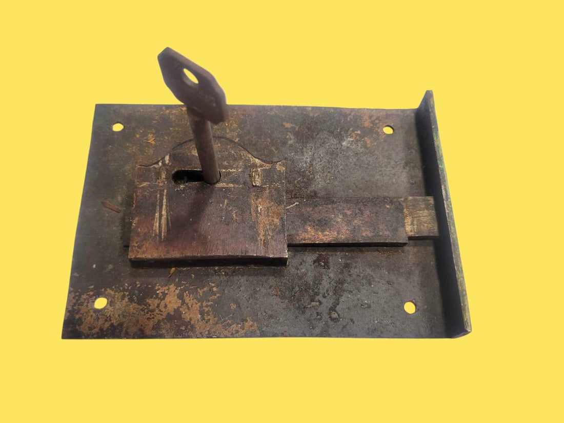Cerradura de forja antigua con llave original sobre fondo amarillo. Ideal para decoración rústica o restauración de puertas vintage.