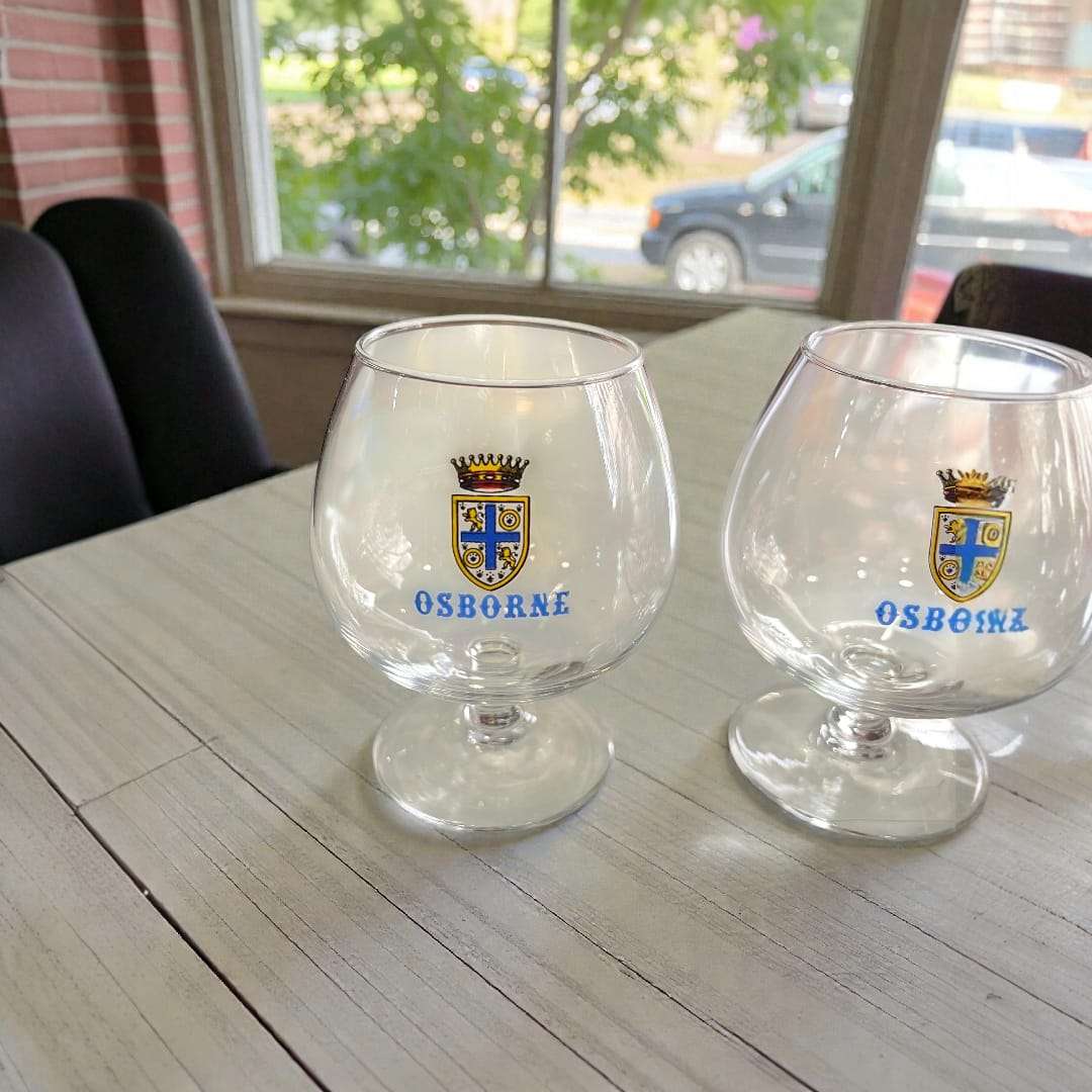 Detalle de copas antiguas de coñac Osborne años 70 con escudo azul y dorado, perfectas para colección o decoración retro en cristalería.