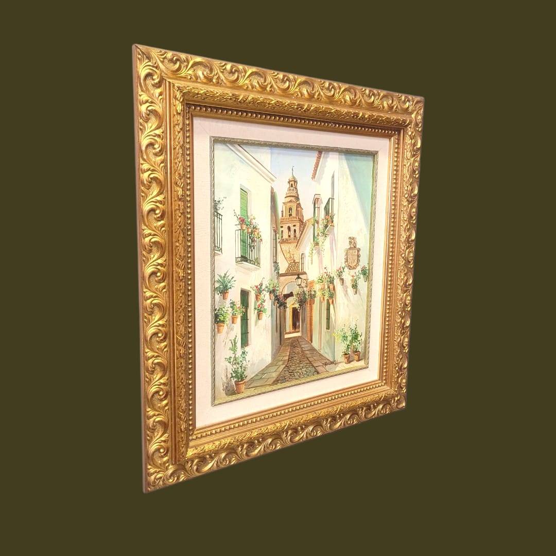 Cuadro al óleo Retamero – Calle típica andaluza con flores y torre al fondo, enmarcado en marco dorado tallado, ideal para decoración de hogar.
