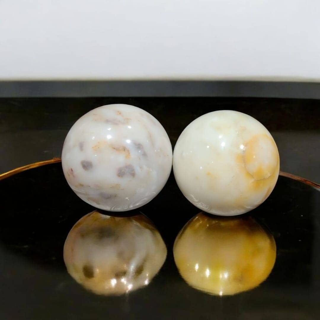 Esferas de mármol macizo decorativas para tu hogar con vetas naturales en tonos beige y blanco, sobre superficie negra brillante.
