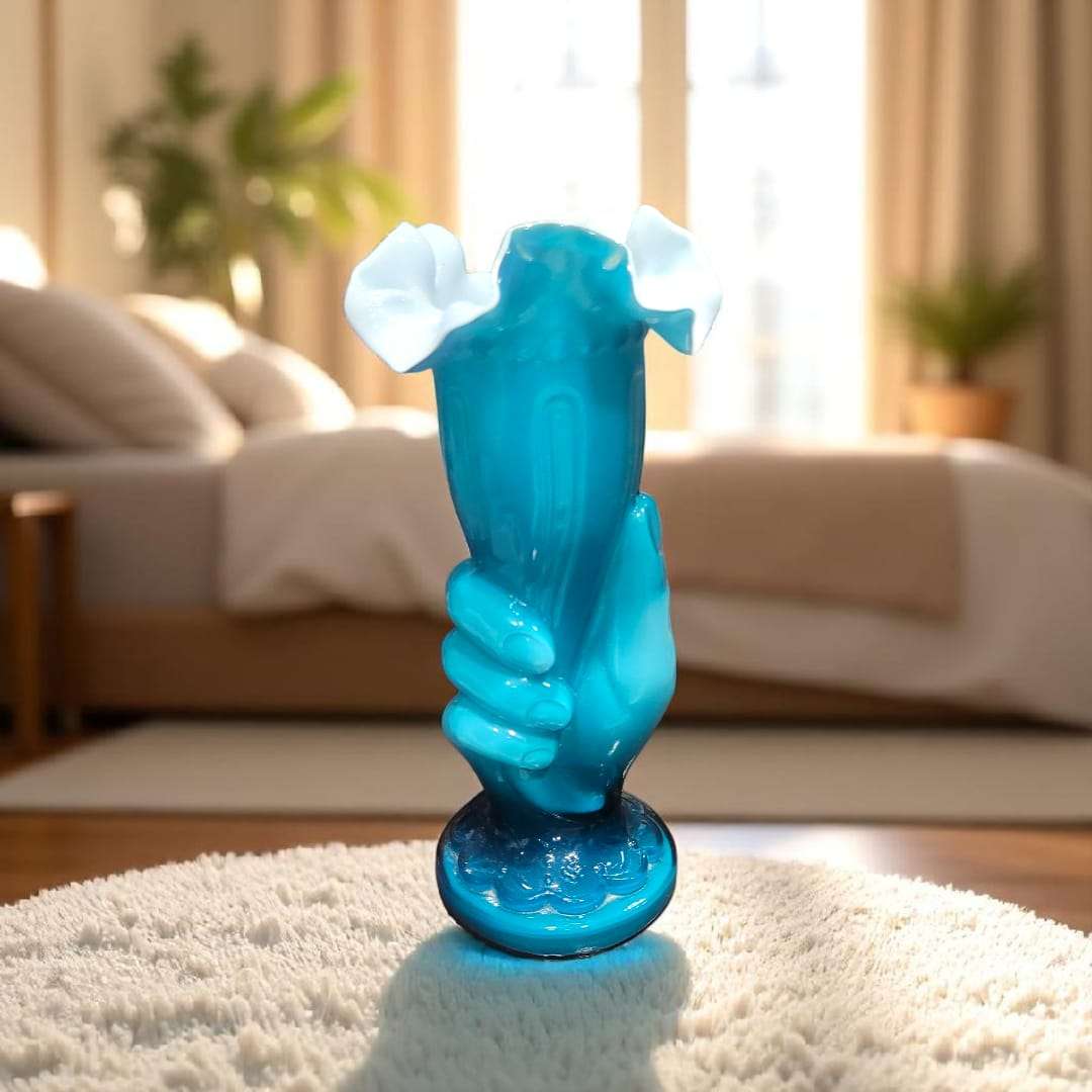 Florero de mano de cristal cuajado azul, sobre alfombra, con fondo de dormitorio.