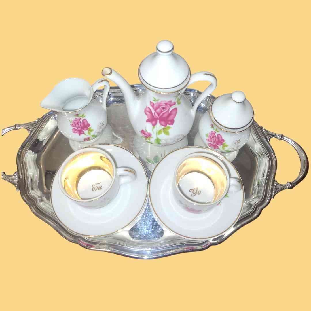 Juego de café 'Tú y Yo' de porcelana con detalles dorados y diseño floral, incluye tazas, platillos, jarra y azucarero.