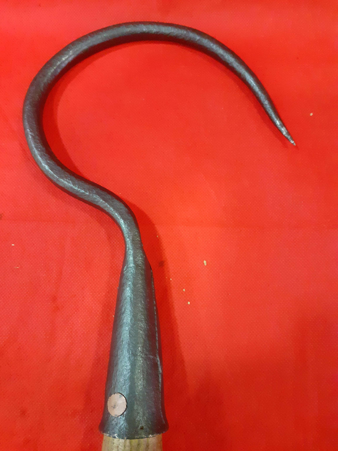 Garfio de hierro antiguo con mango de madera sobre fondo rojo, ideal para decoración rústica o coleccionistas. Disponible en Cositas Antiguas.