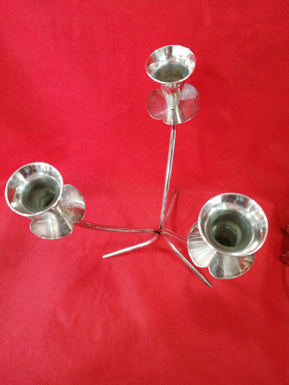 Pareja de candelabros de alpaca de 33 cm con diseño curvo y elegante sobre fondo rojo. Decoración ideal para espacios sofisticados y modernos.