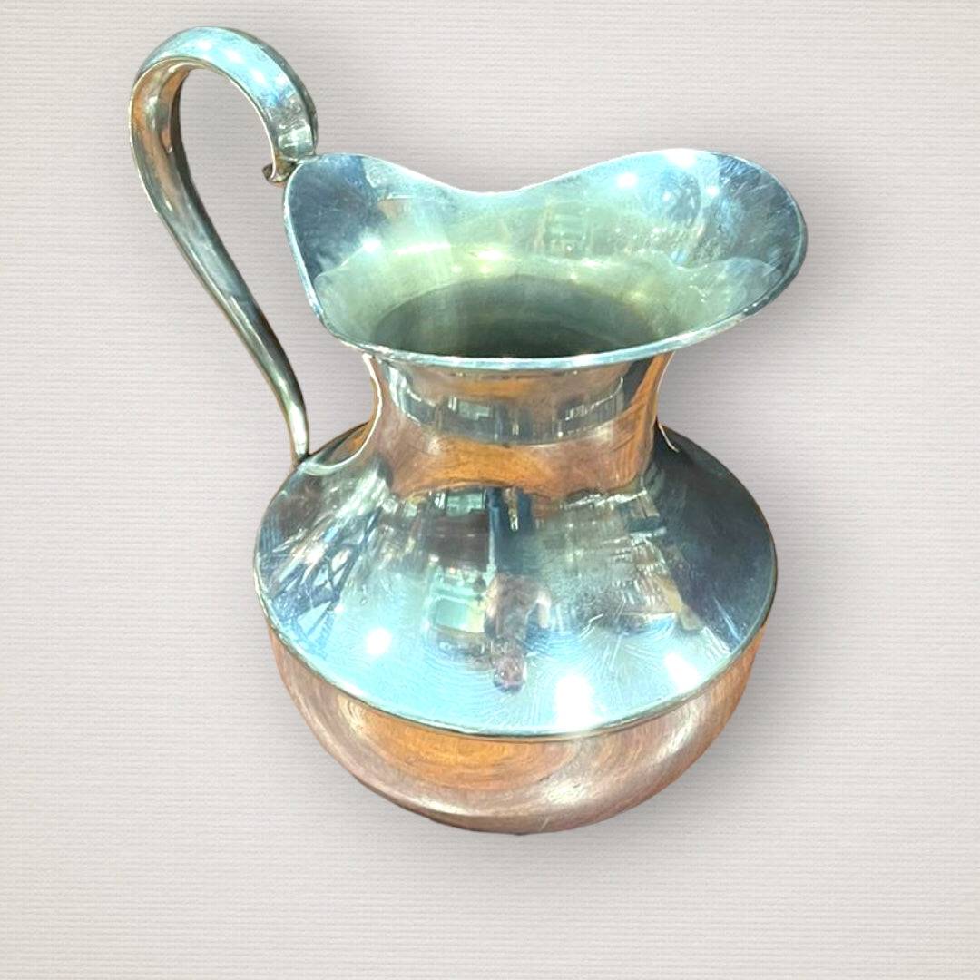 Jarra elegante de metal plateado con diseño curvo y acabado brillante, ideal para decoración de comedor o mesa en estilo clásico.