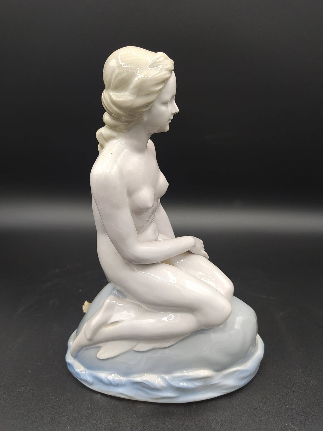 Figura de La Sirenita de porcelana en posición sentada sobre una roca, con acabado brillante y estilo clásico, ideal para decoración vintage.